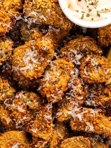 A platter of crispy artichoke hearts with lemon wedges, parmesan garnish, and a small bowl of garlic aioli.