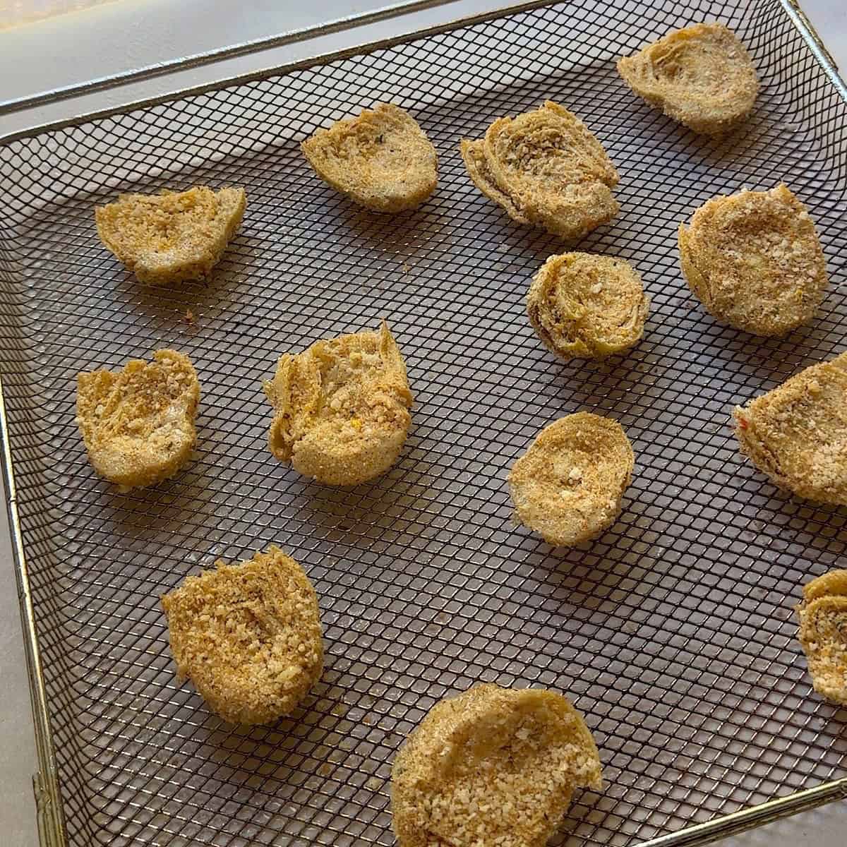 Coated artichoke hearts on an air fryer tray.