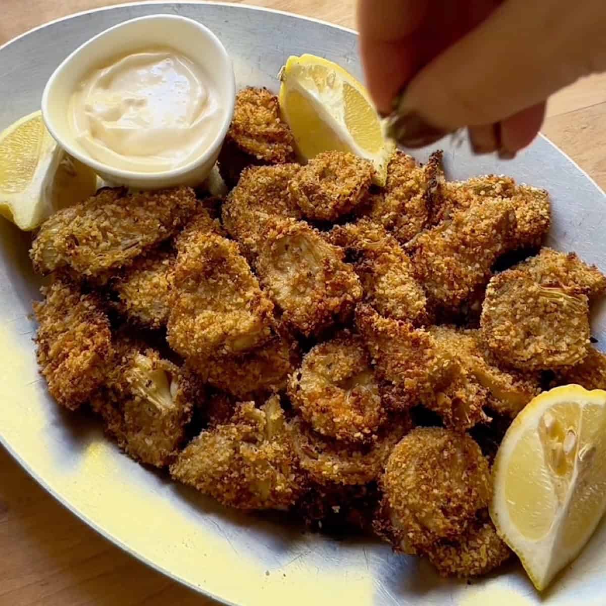 Adding seasoning to a tray of crispy air-fried artichoke hearts.