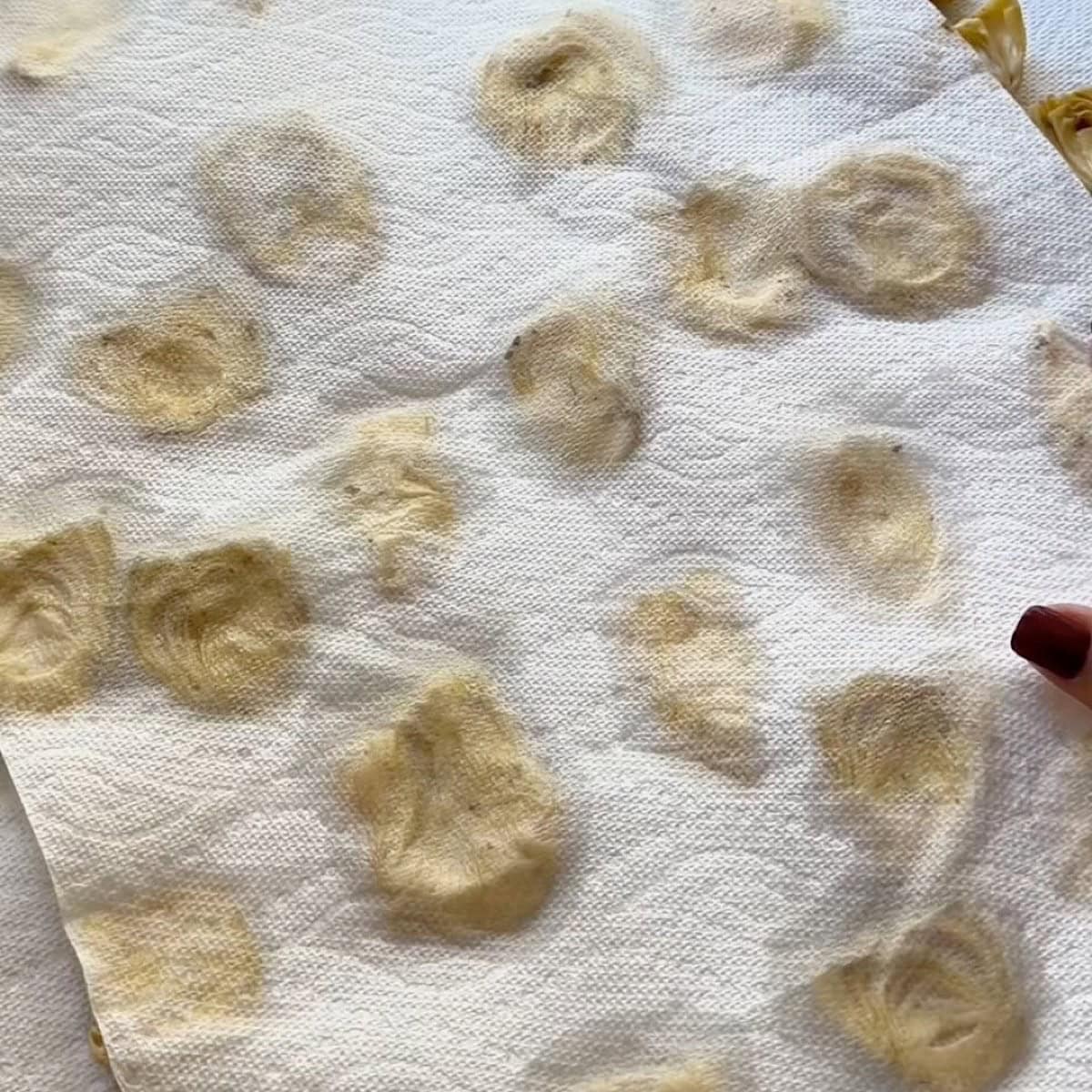 Artichoke hearts on a sheet pan with paper towels pressed on top.