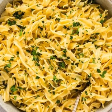 A bowl of buttered egg noodles topped with parsley.