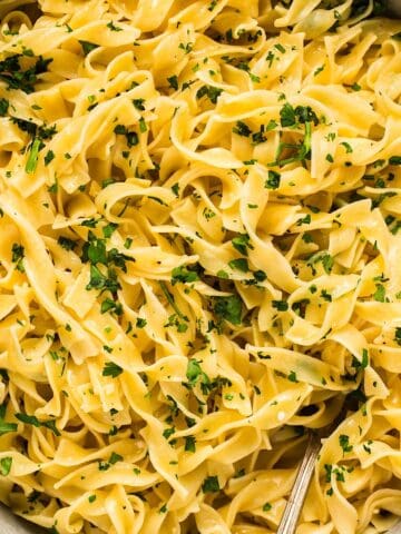 A bowl of buttered egg noodles topped with parsley.