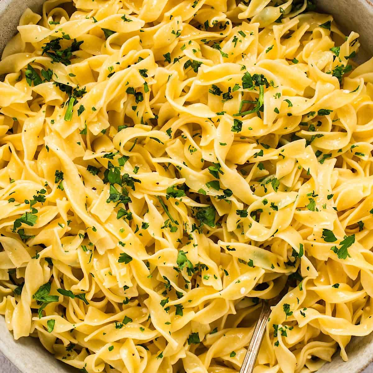 A bowl of buttered egg noodles topped with parsley.