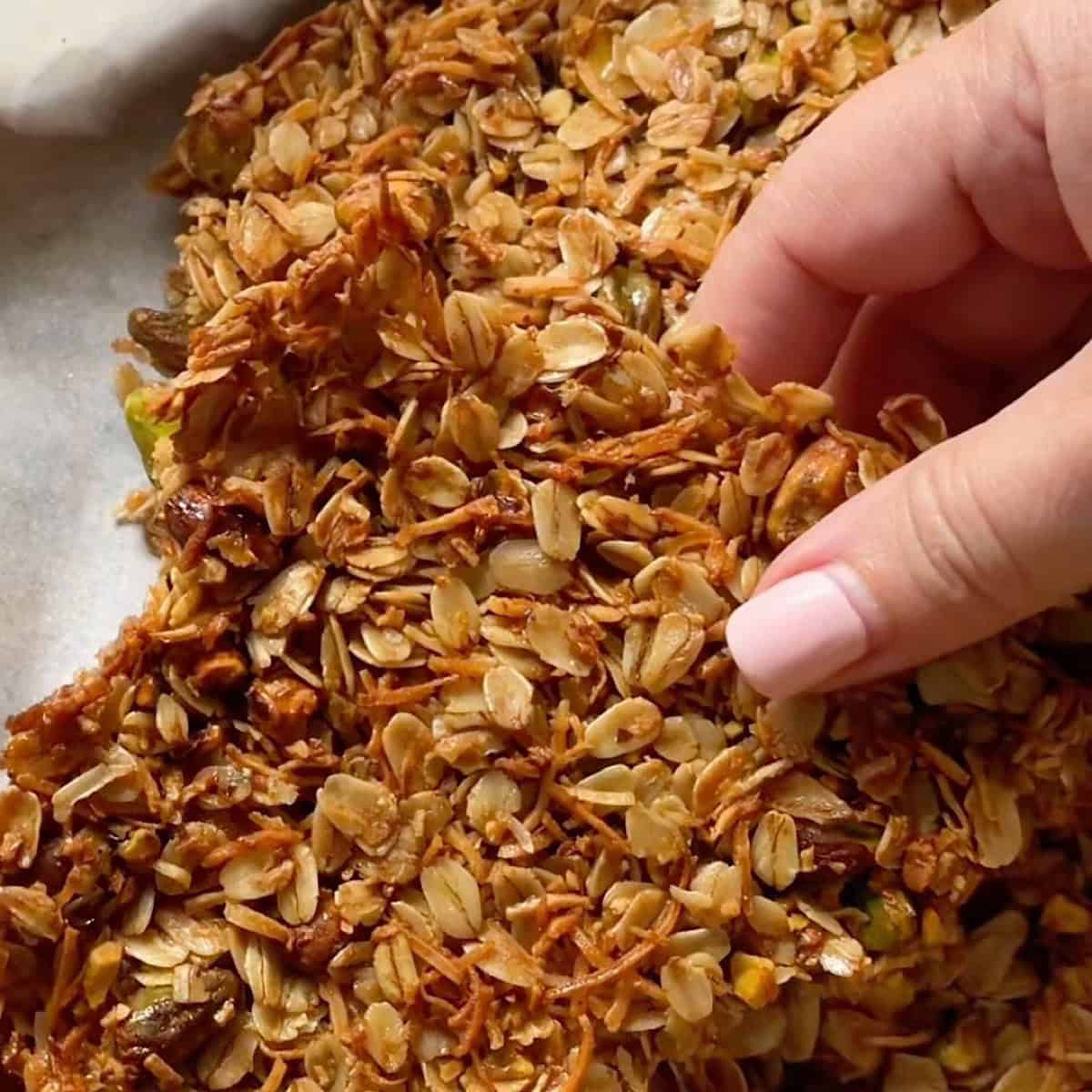 Breaking a cluster of the baked honey granola on the sheet pan.
