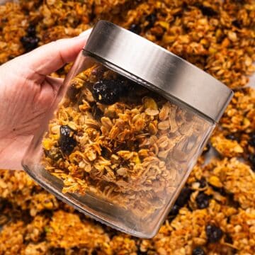 Holding a jar of homemade honey granola over the sheet pan of granola.