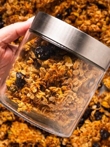 Holding a jar of homemade honey granola over the sheet pan of granola.