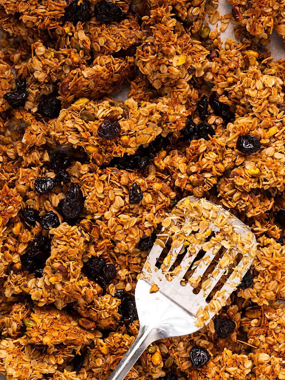 A sheet pan of honey almond granola with a spatula for serving.