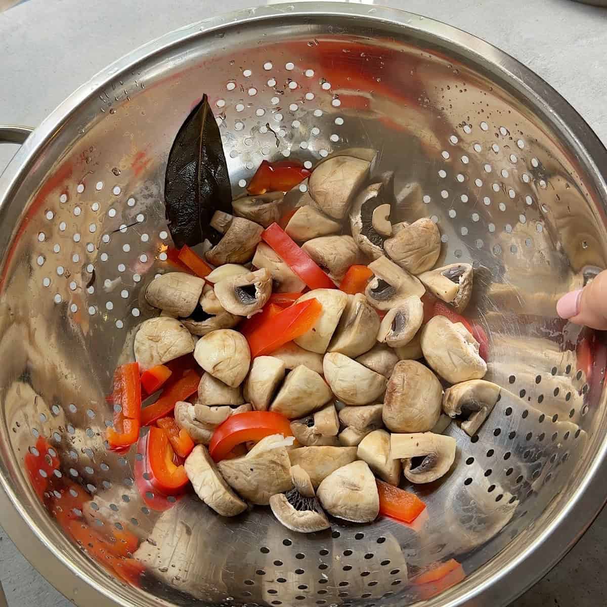 Mushrooms and peppers drained in a colander.