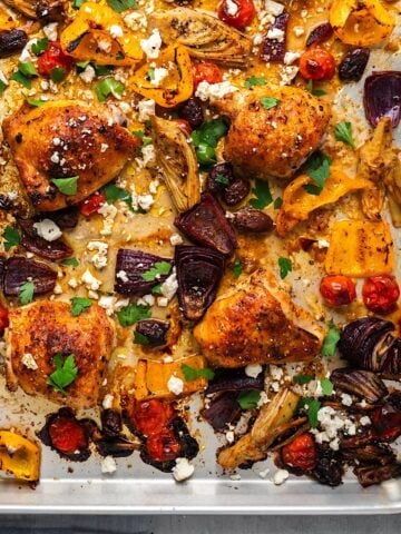 Roasted Mediterranean chicken and vegetables on a sheet pan with feta cheese and parsley.