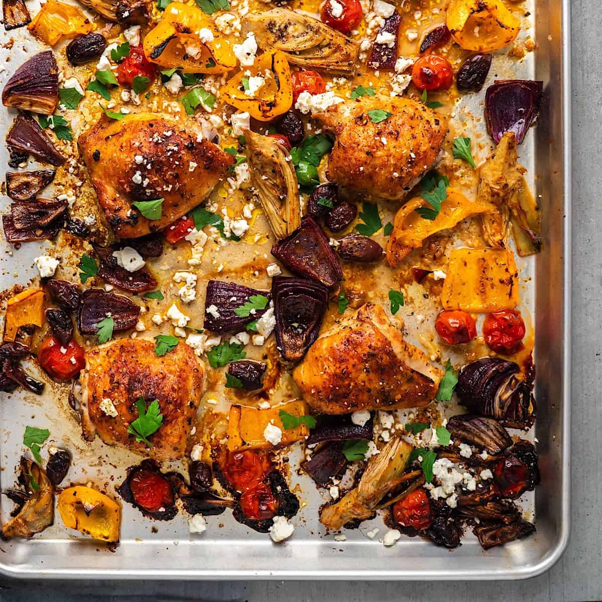 Roasted Mediterranean chicken and vegetables on a sheet pan with feta cheese and parsley.