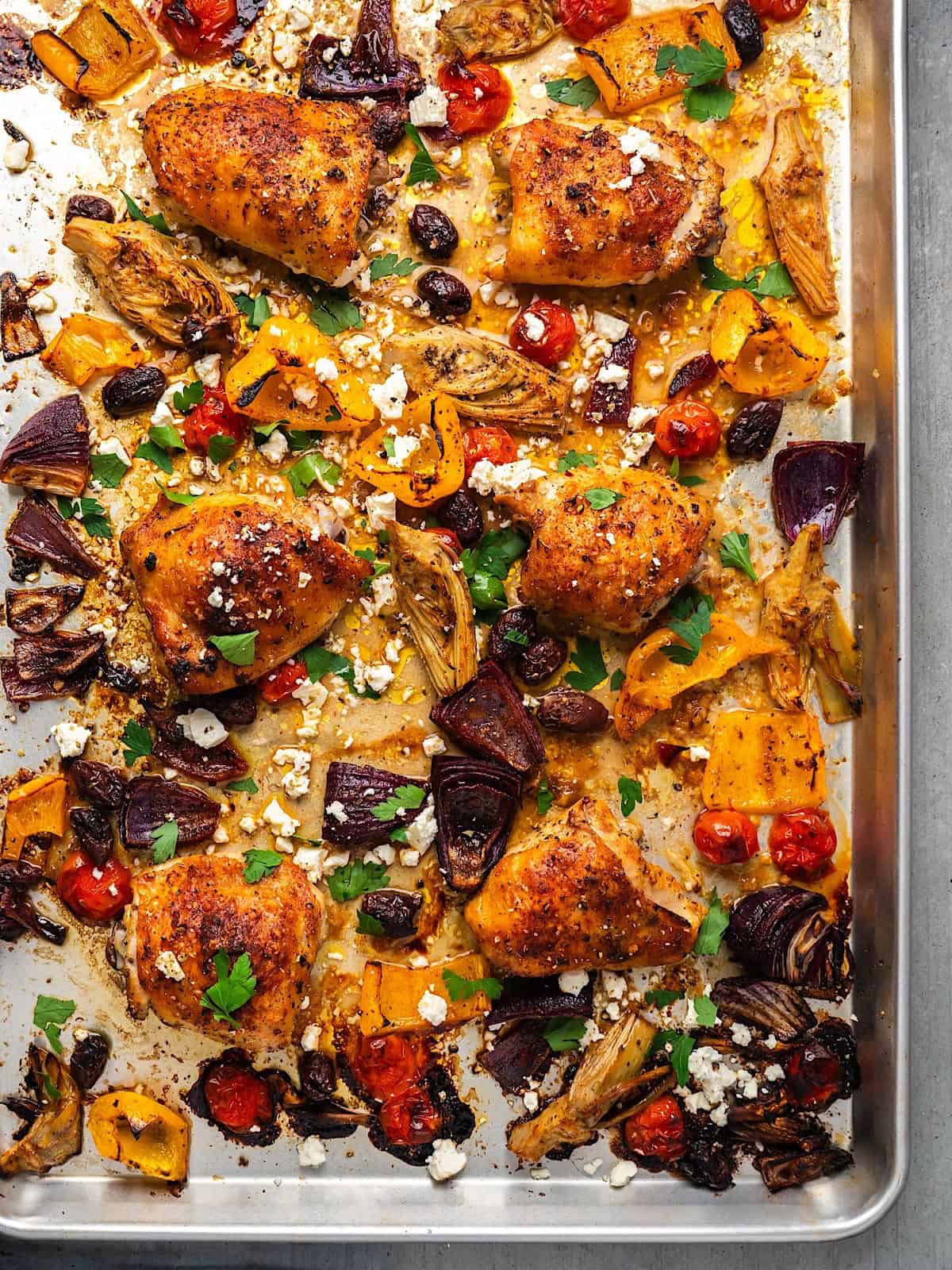 Roasted Mediterranean chicken and vegetables on a sheet pan with feta cheese and parsley.