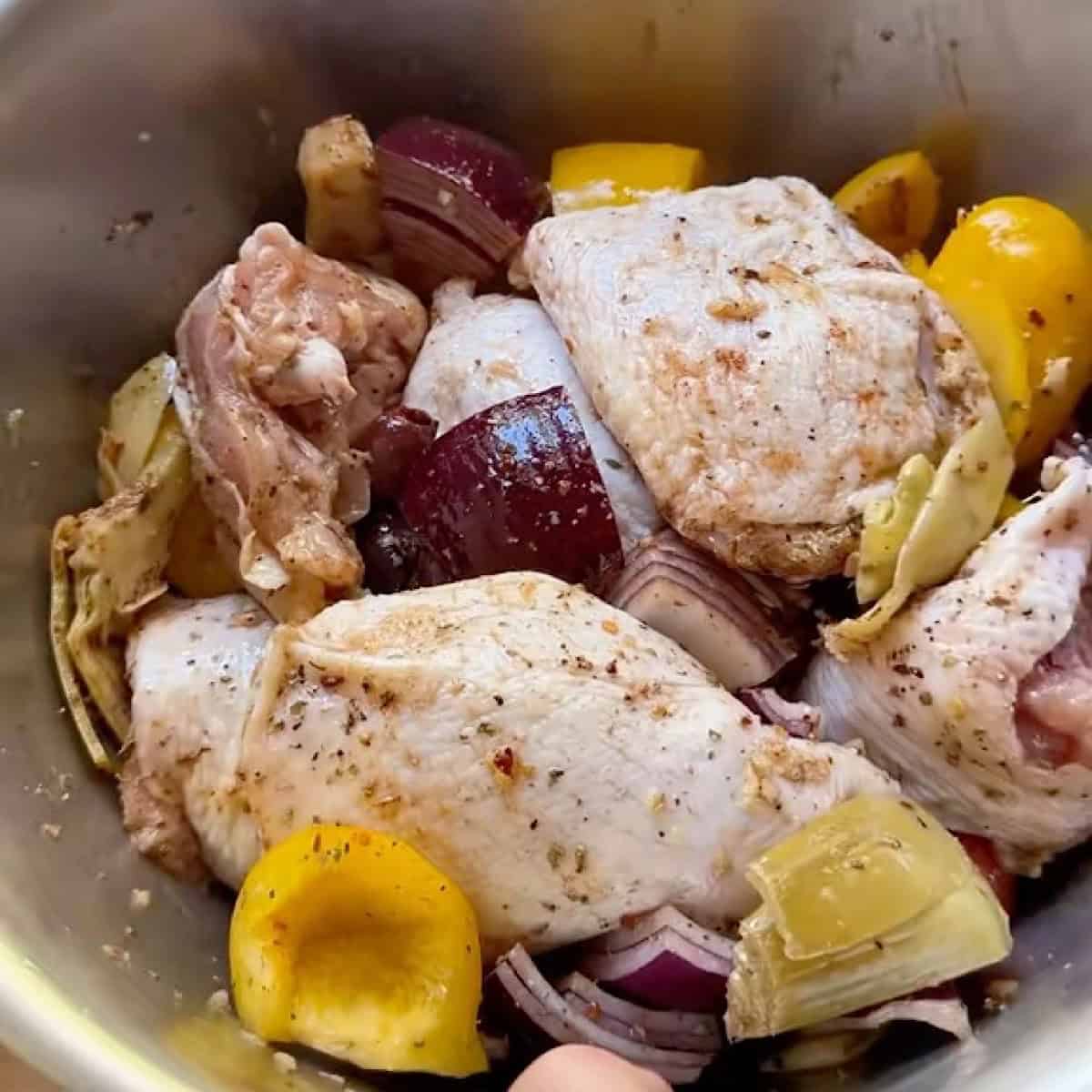 Tossed chicken, vegetables, and seasoning in a mixing bowl.