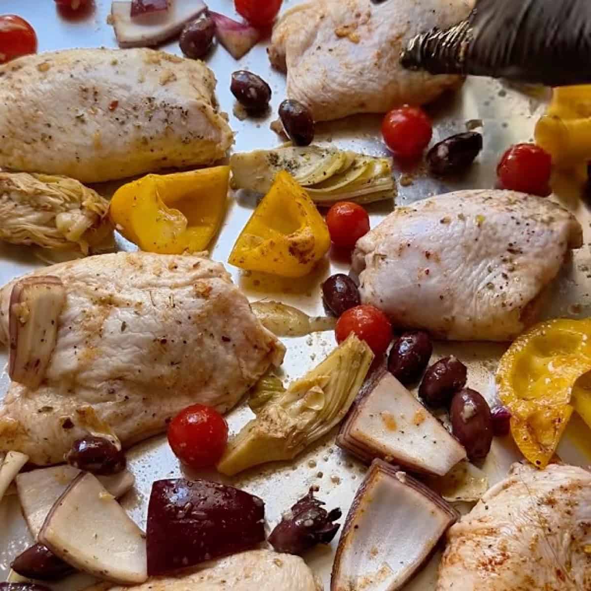 Sheet pan arranged with chicken and vegetables evenly spaced apart.