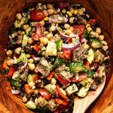 Steak chimichurri dense bean salad tossed in a wooden bowl with wooden spoon.