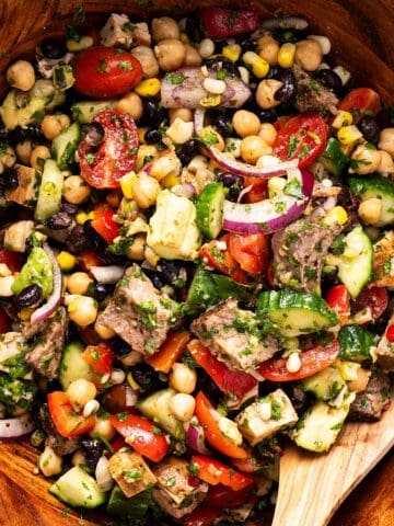 Steak chimichurri dense bean salad tossed in a wooden bowl with wooden spoon.