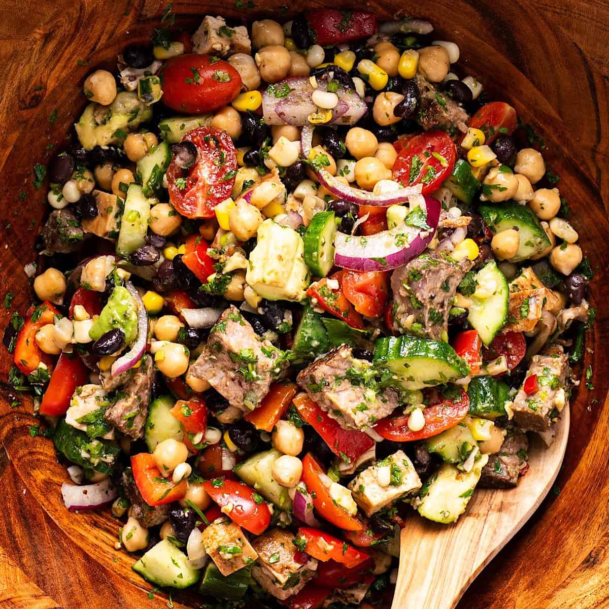 Steak chimichurri dense bean salad tossed in a wooden bowl with wooden spoon.
