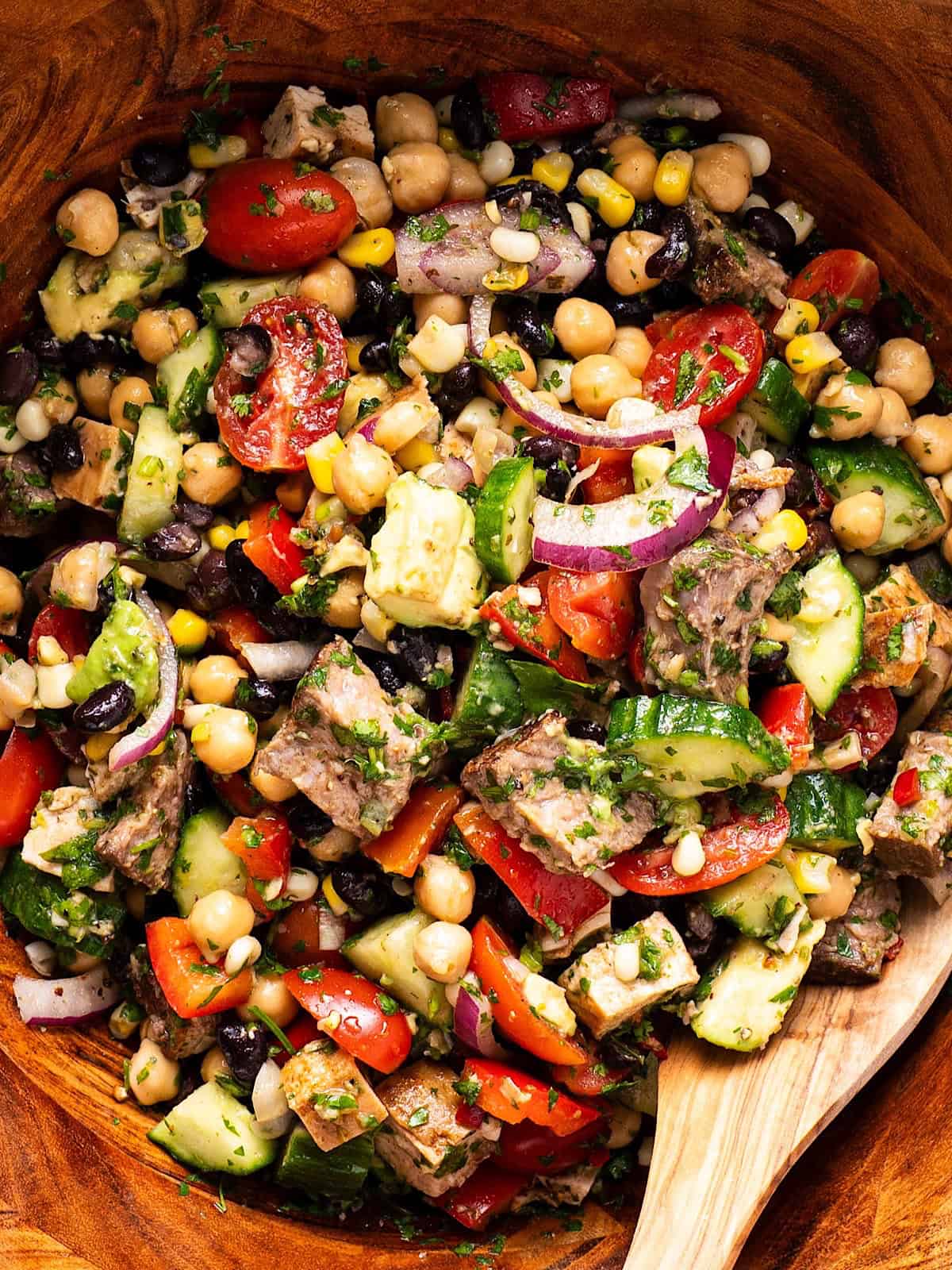 Steak chimichurri dense bean salad tossed in a wooden bowl with wooden spoon.