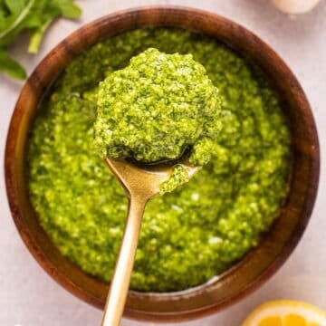 A gold spoonful of basil arugula pesto over a wooden bowl of pesto.