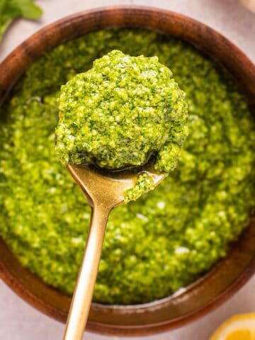 A gold spoonful of basil arugula pesto over a wooden bowl of pesto.