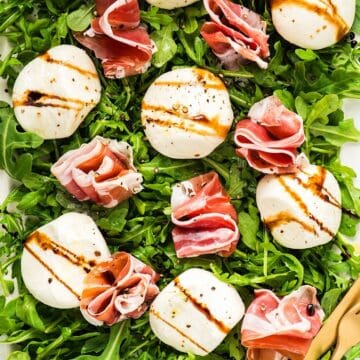 Burrata and prosciutto on a platter of arugula dressed with olive oil and balsamic glaze.