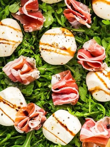 Burrata and prosciutto on a platter of arugula dressed with olive oil and balsamic glaze.
