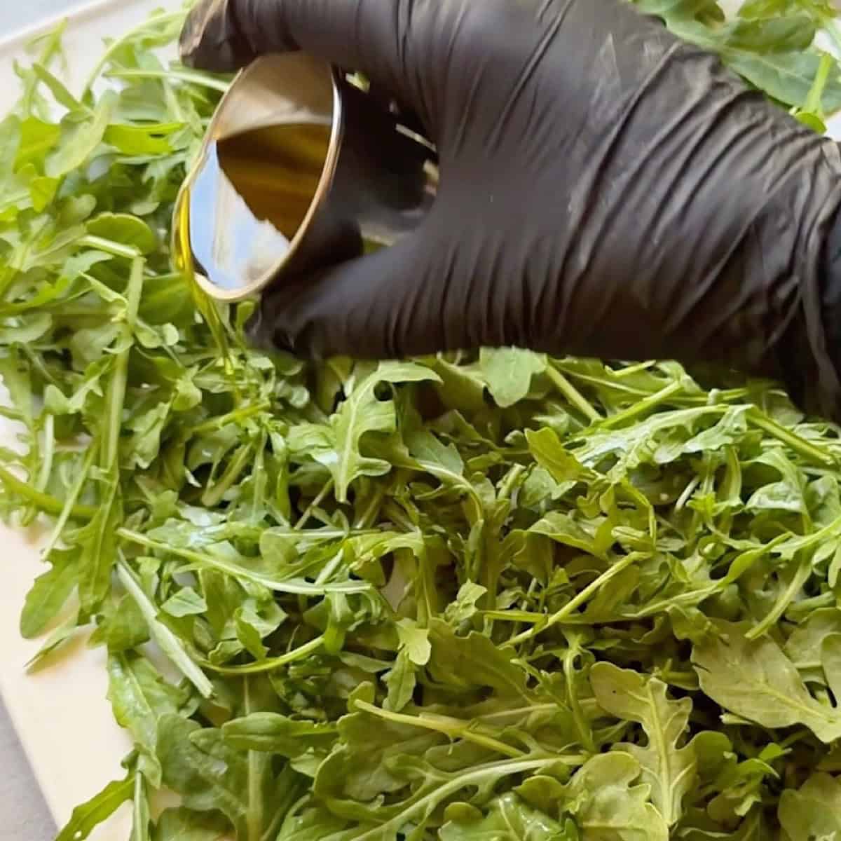 Drizzling olive oil over a bed of arugula lettuce.