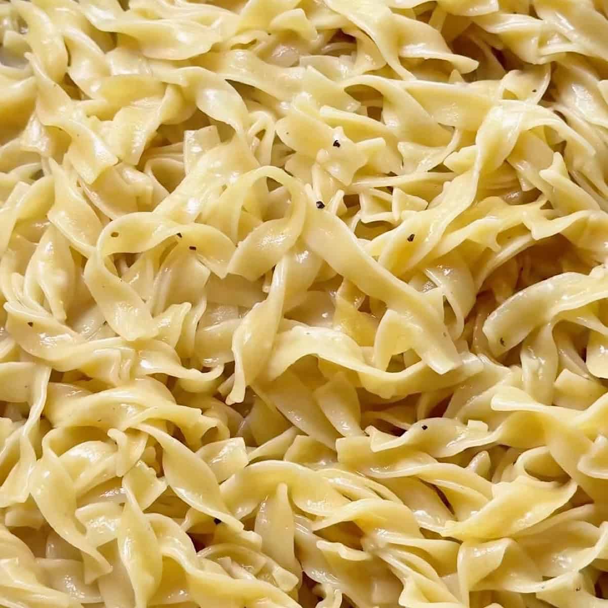 Tossed egg noodles with butter and seasoning in a skillet.