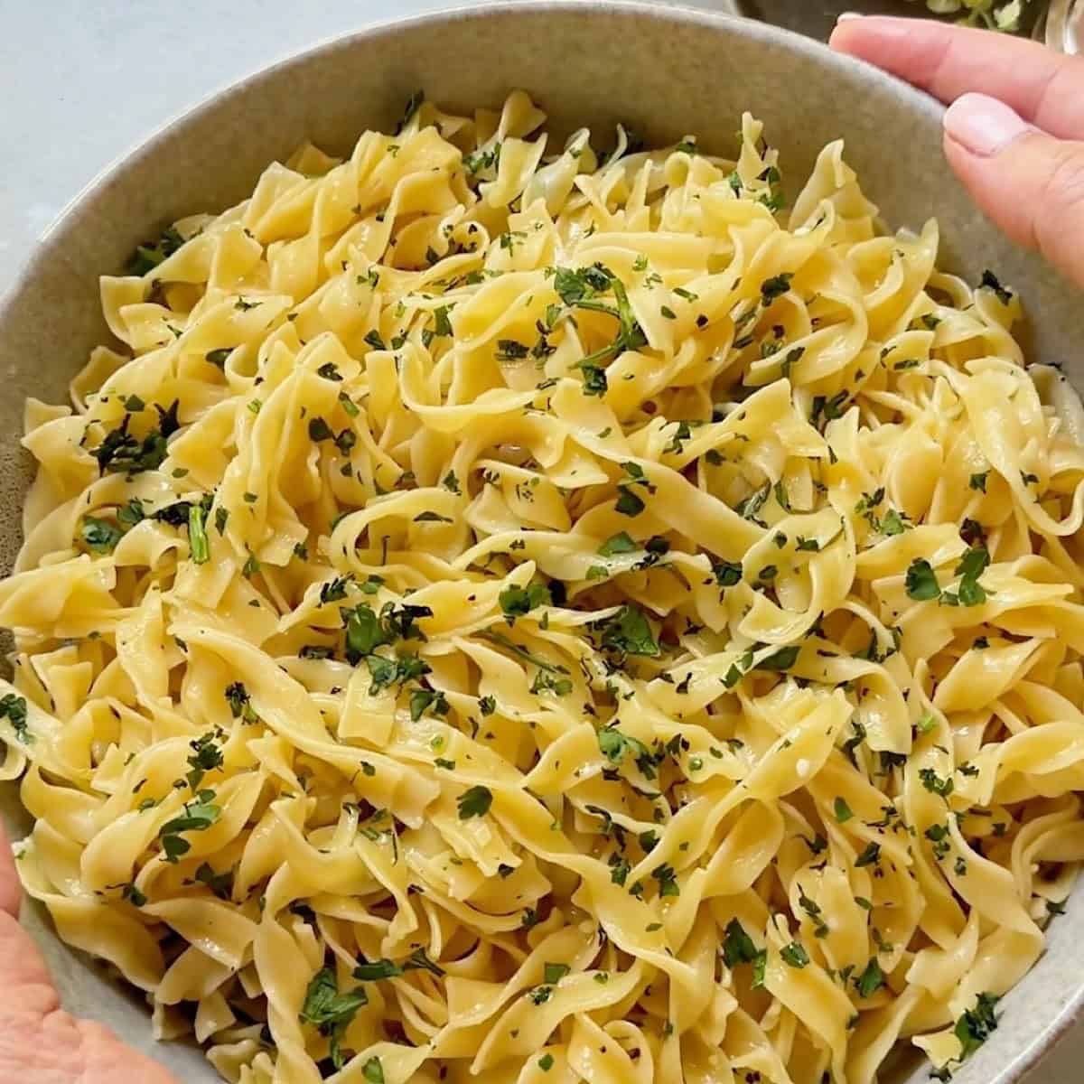 Holding buttered egg noodles with parmesan in a bowl garnished with parsley.