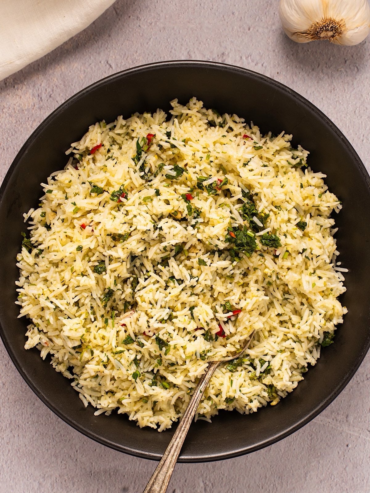 Chimichurri rice in a black bowl next to linen and garlic bulb.