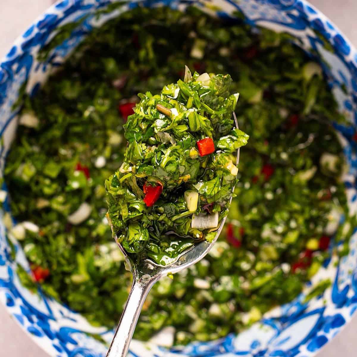 A spoonful of cilantro chimichurri sauce being held over a decorative blue bowl.