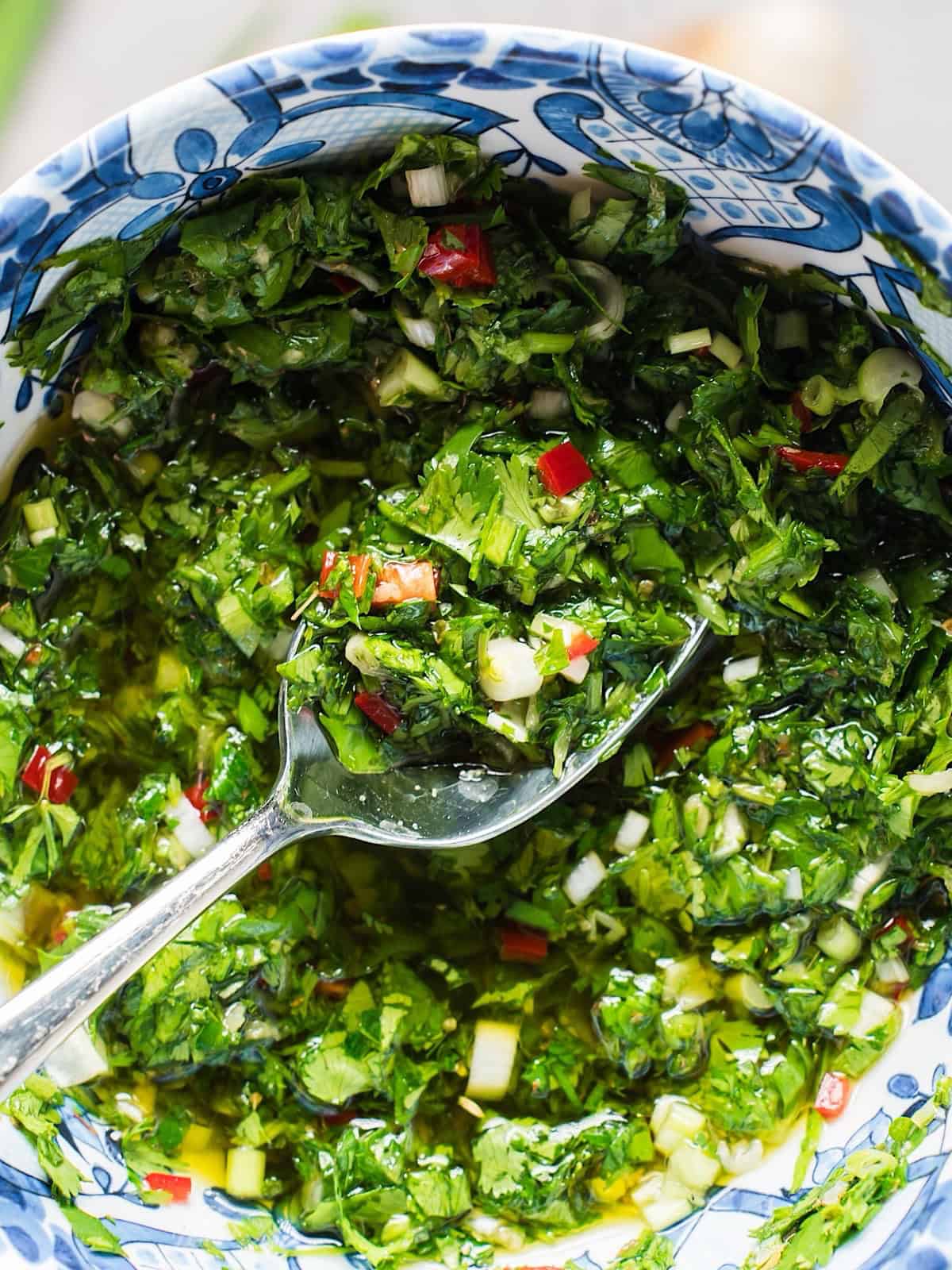 A decorative blue bowl of cilantro with a spoon dipped in it to show texture.