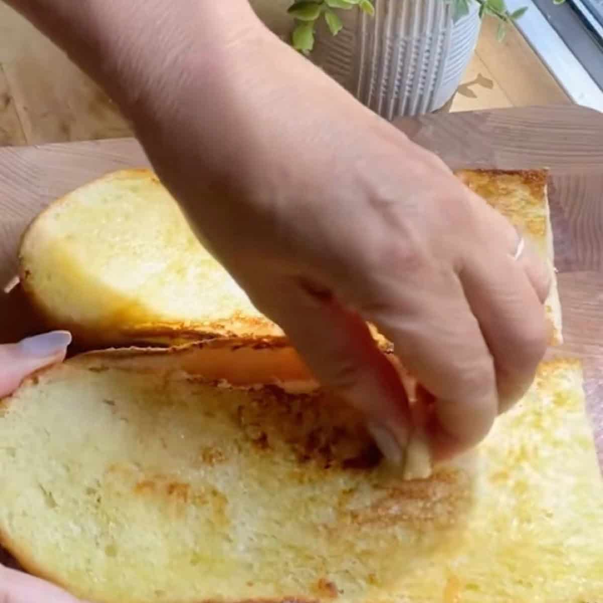 Rubbing a garlic clove over an open faced toasted french loaf.
