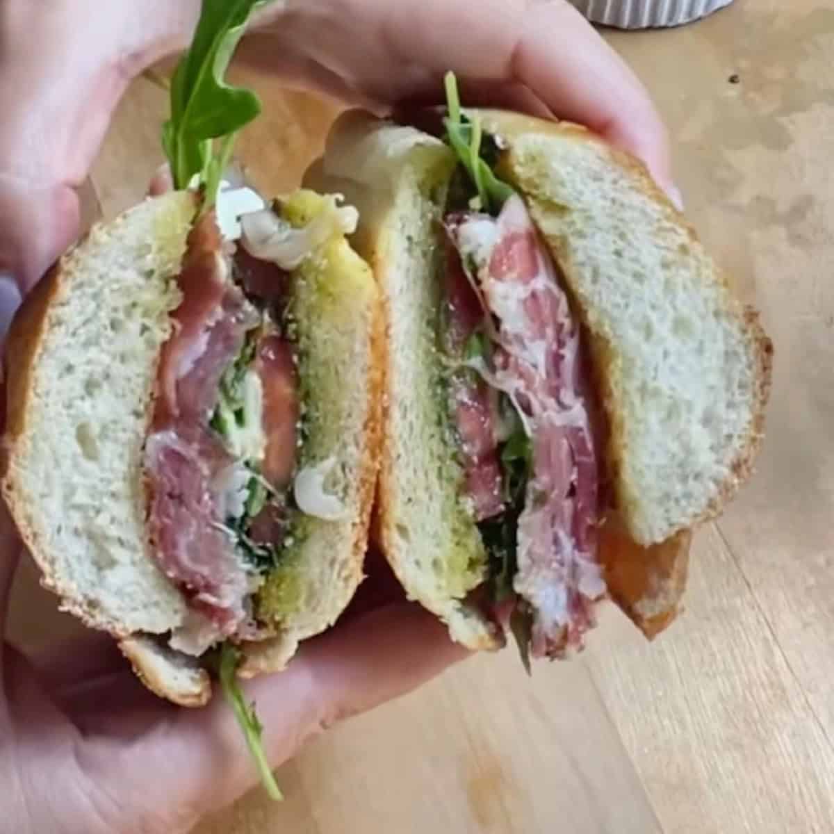 Holding the sliced pesto caprese sandwich to show the inside.