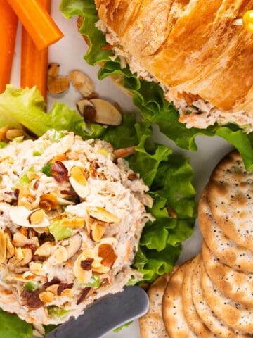 An mount of honey chicken salad with a croissant sandwich, crackers, and carrot sticks.