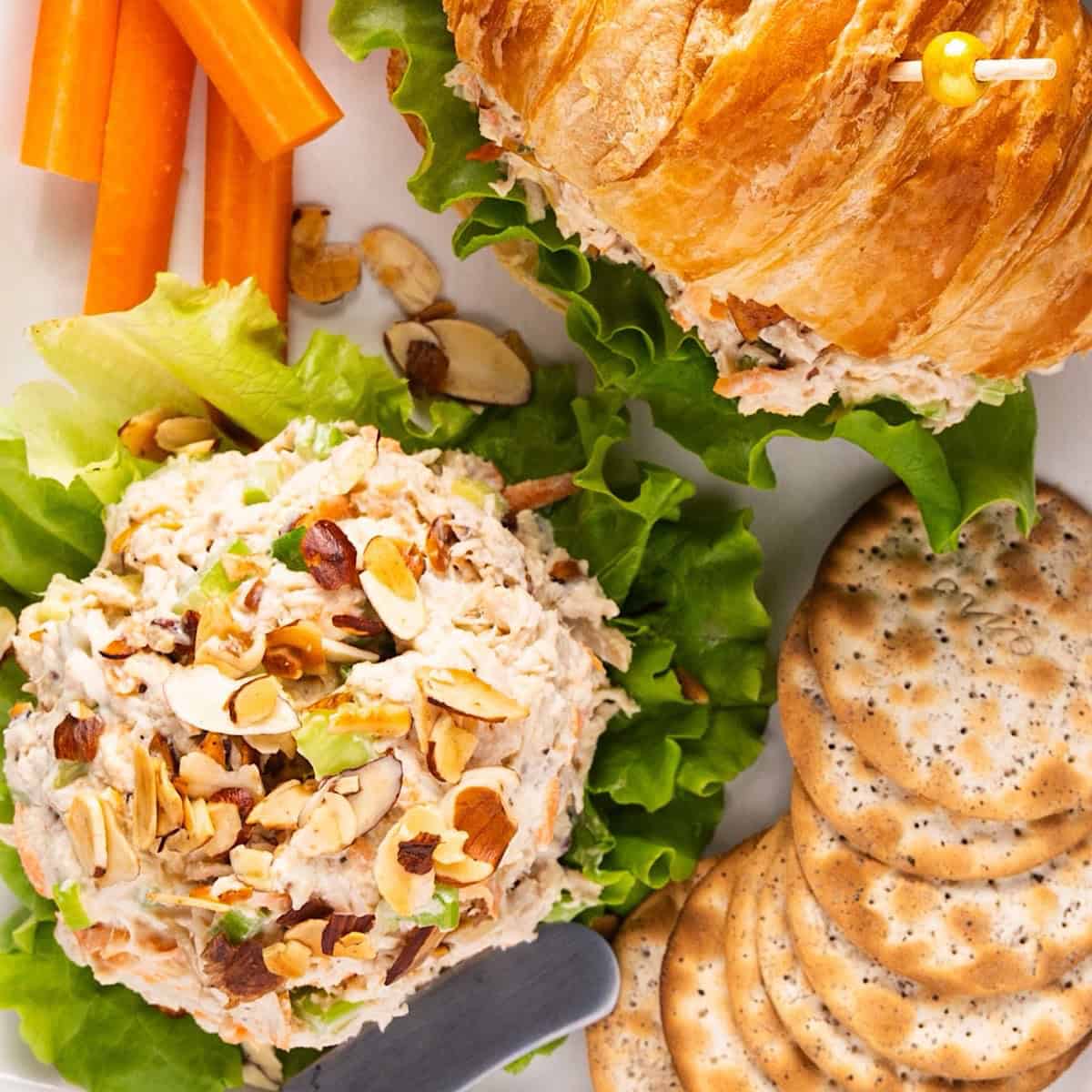 An mount of honey chicken salad with a croissant sandwich, crackers, and carrot sticks.