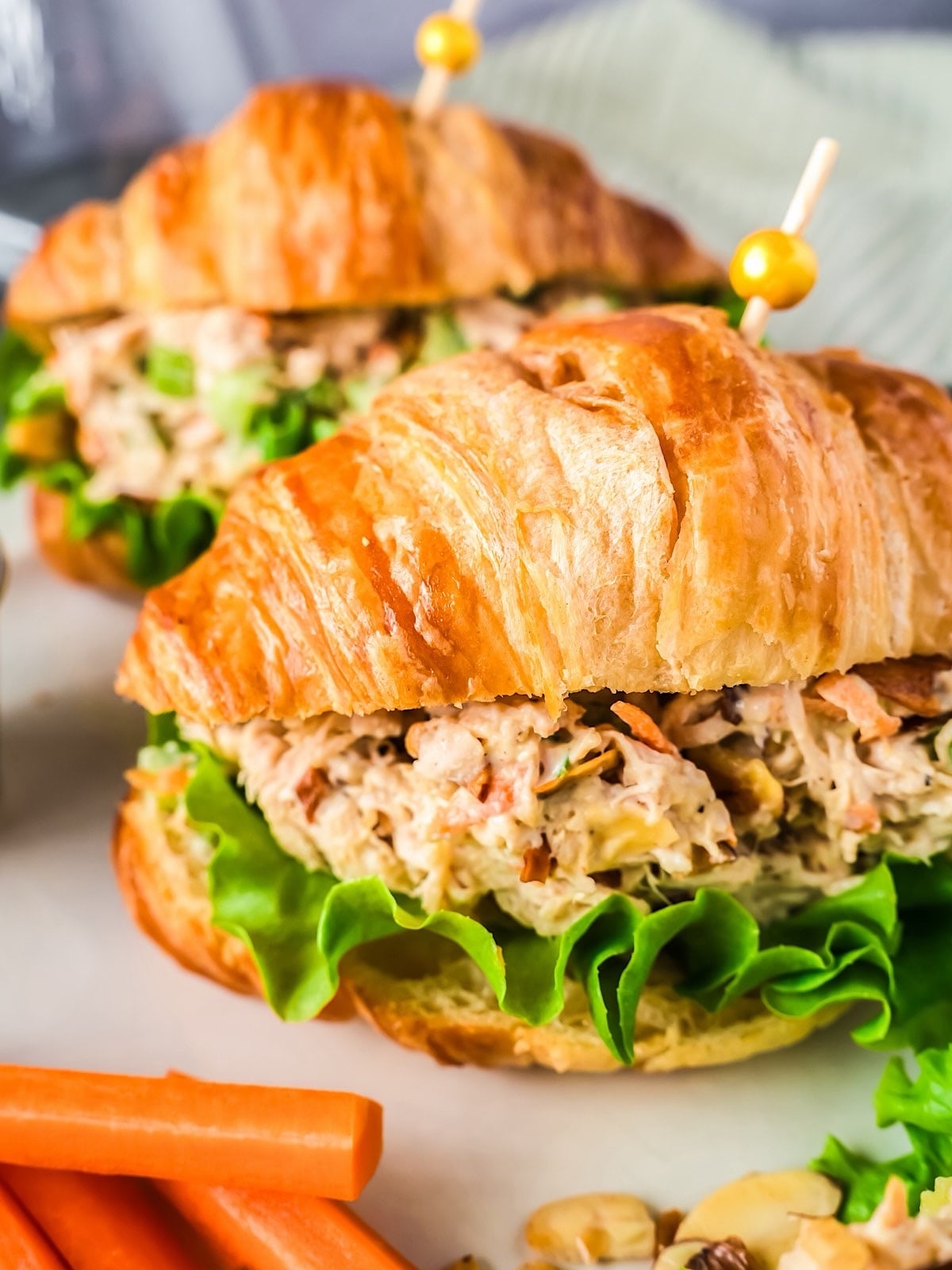 Two honey chicken salad sandwiches in croissants with party picks and curly lettuce.