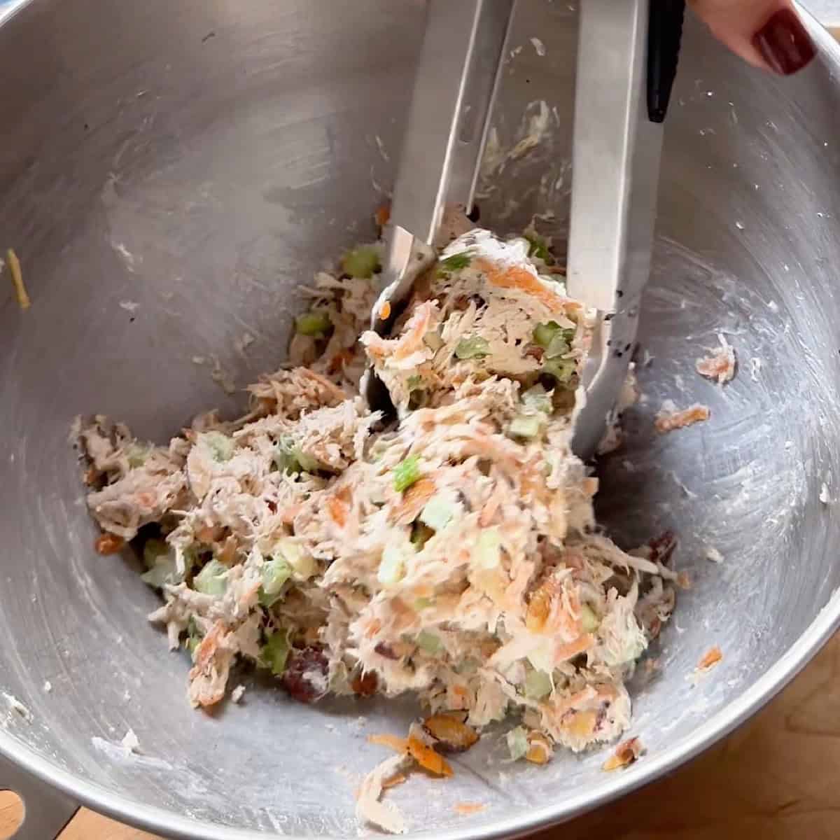 Folding the honey chicken salad with tongs to coat.