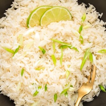 Fluffy and creamy Instant pot coconut rice in a black bowl with green onions and lime as garnish.