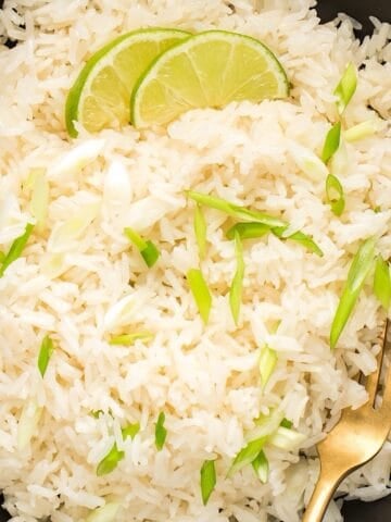 Fluffy and creamy Instant pot coconut rice in a black bowl with green onions and lime as garnish.