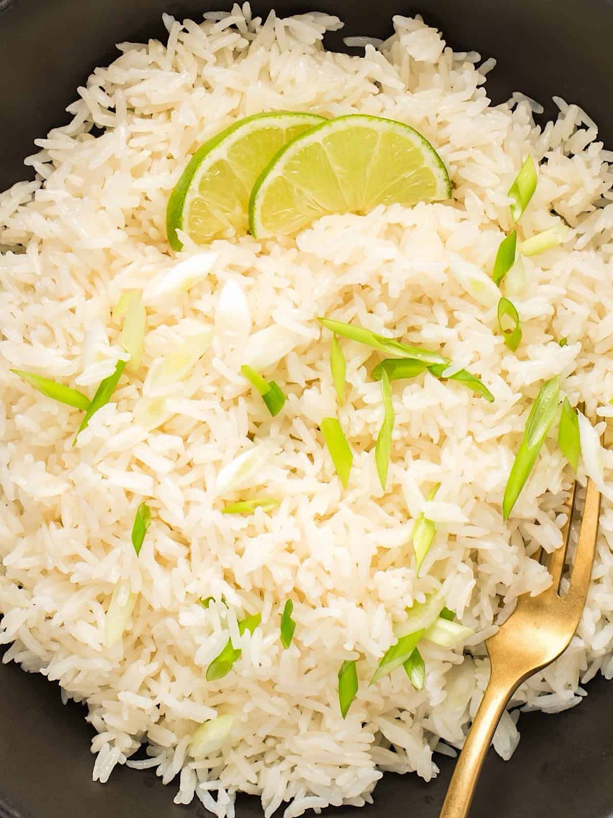 Instant pot coconut rice in black bowl with gold fork and garnishes.
