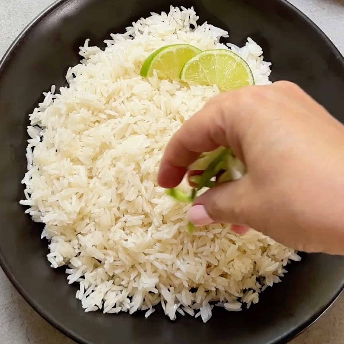 Adding green onion and lime to a bowl of creamy and fluffy coconut rice.
