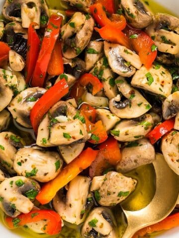 Italian marinated mushrooms in a white bowl with gold spoon.