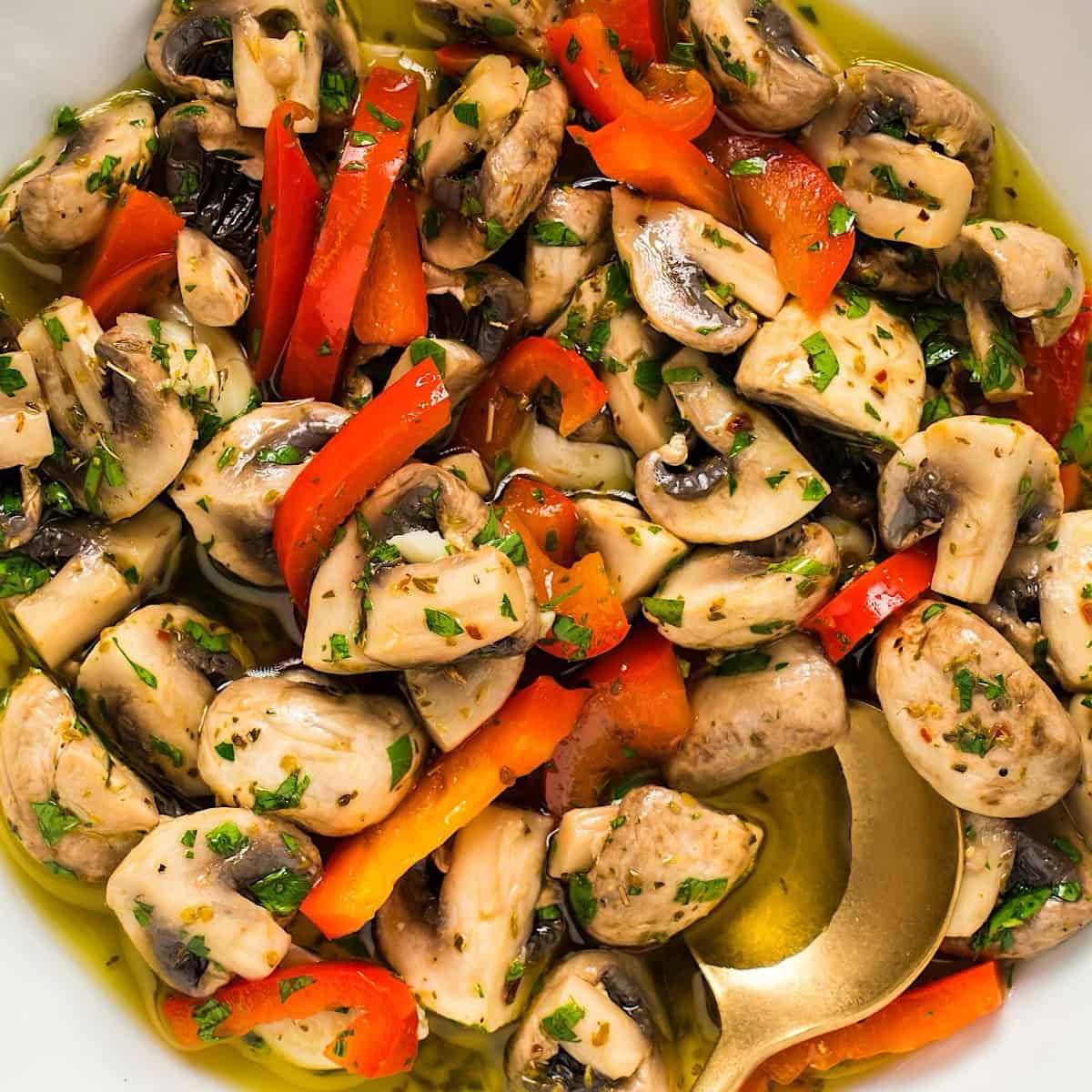 Italian marinated mushrooms in a white bowl with gold spoon.