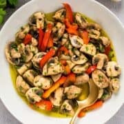 Italian marinated mushrooms in a white bowl with garlic, parsley, and gold spoon for composition.