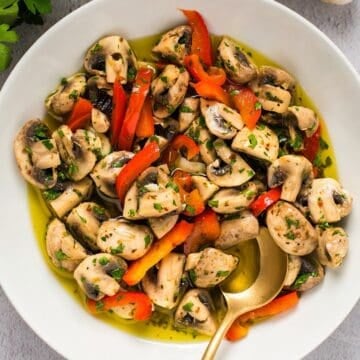 Italian marinated mushrooms in a white bowl with garlic, parsley, and gold spoon for composition.