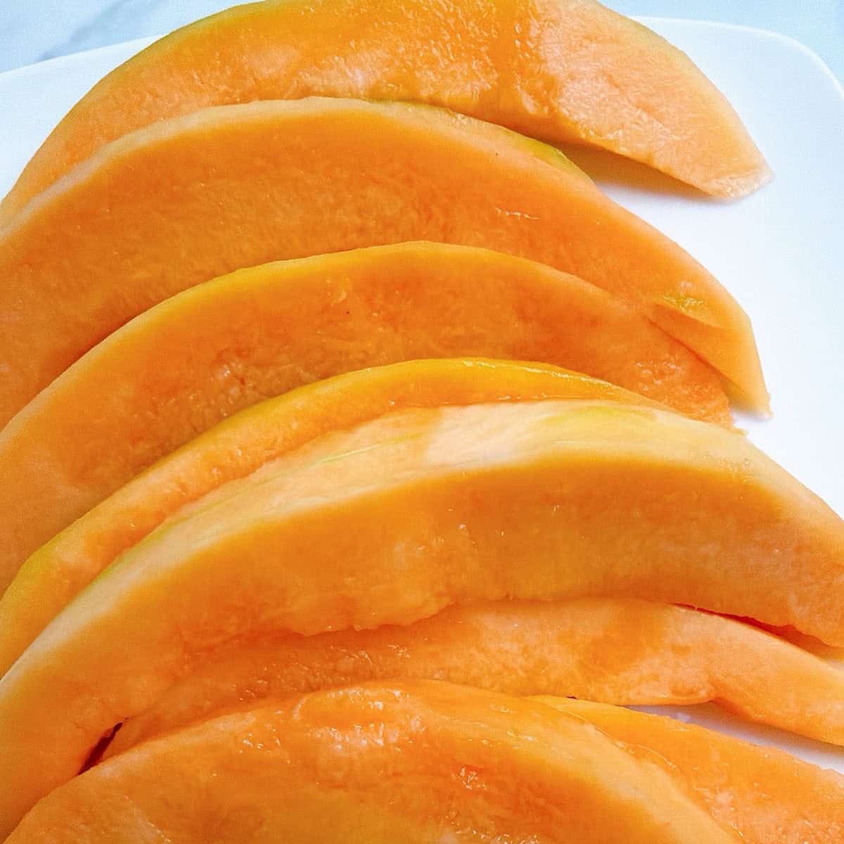 Cantaloupe wedges with outer peel and seeds removed stacked on a plate.