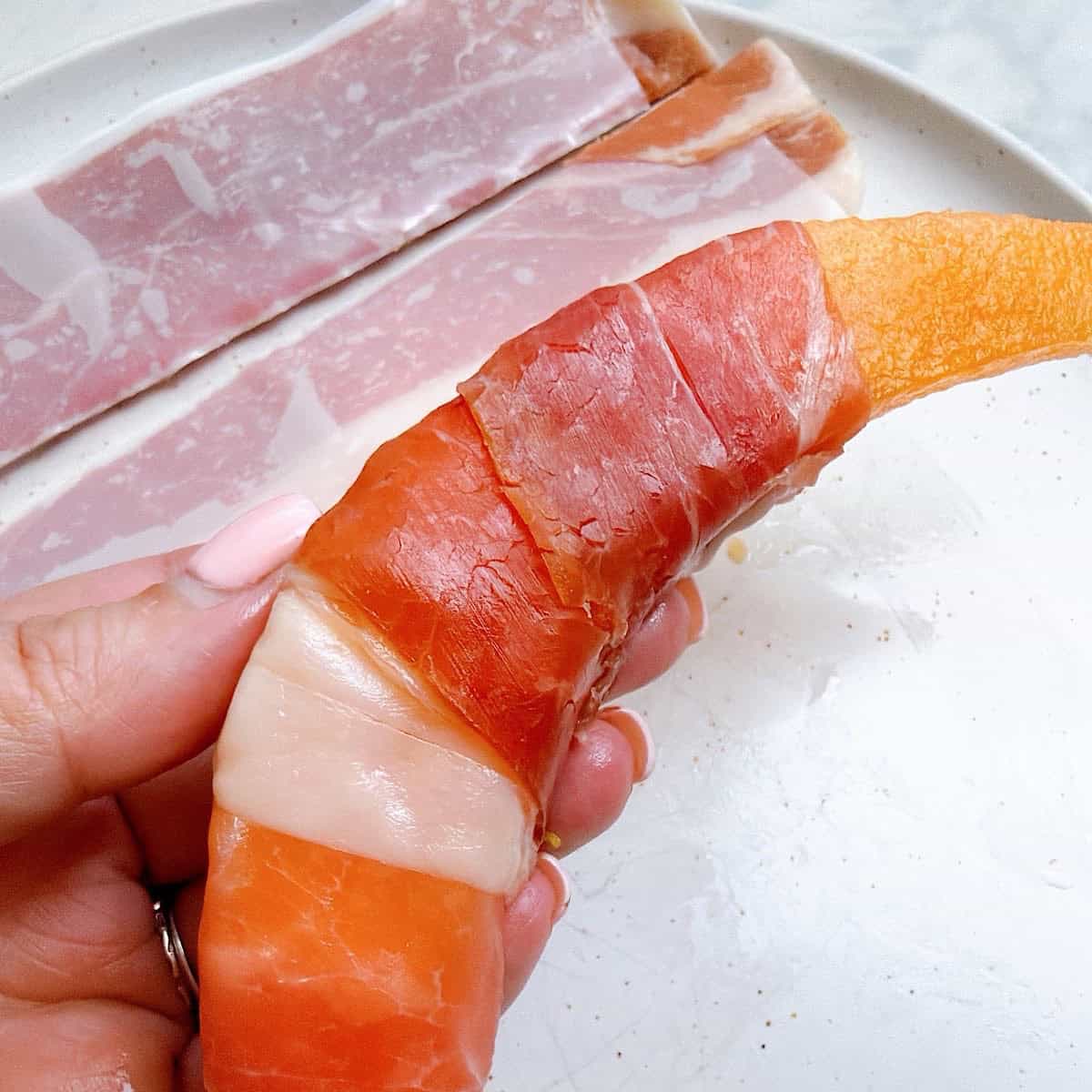 Holding a prosciutto wrapped cantaloupe wedge.
