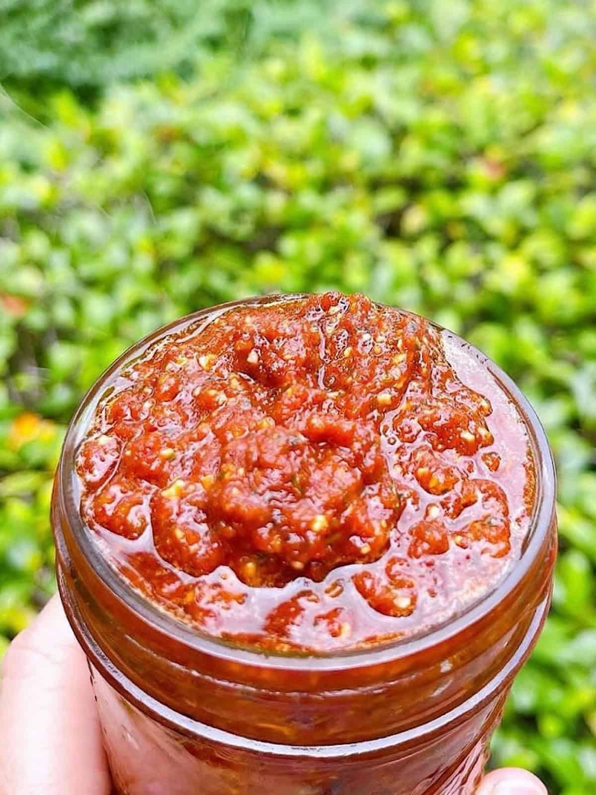 Holding sundried tomato pesto in a jar outside.