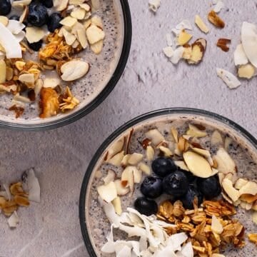 Two bowls of blueberry chia pudding with granola, coconut, and almond toppings.
