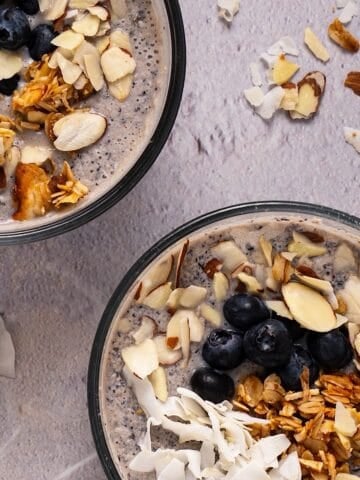 Two bowls of blueberry chia pudding with granola, coconut, and almond toppings.
